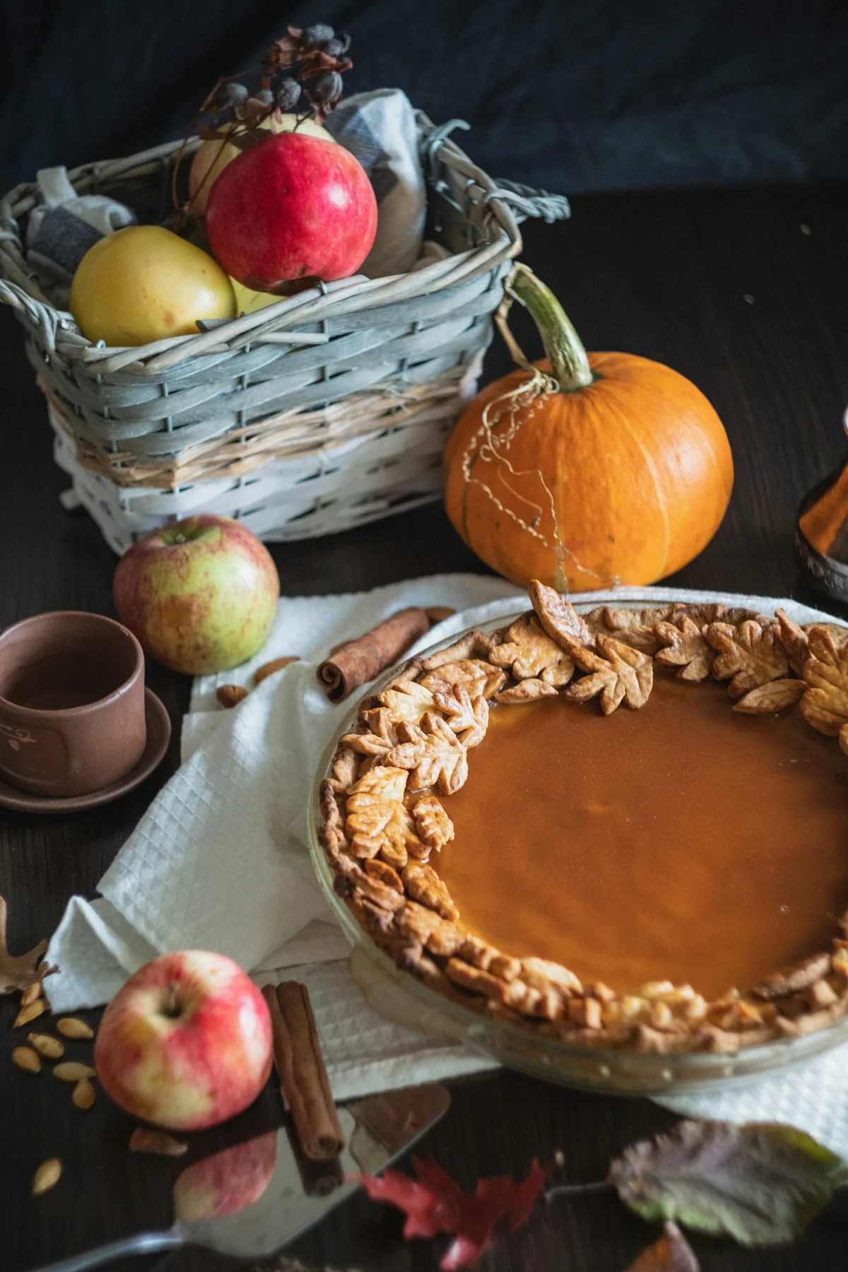 Pumpkin pie with a decorative leaf crust beside a pumpkin and autumn fruit